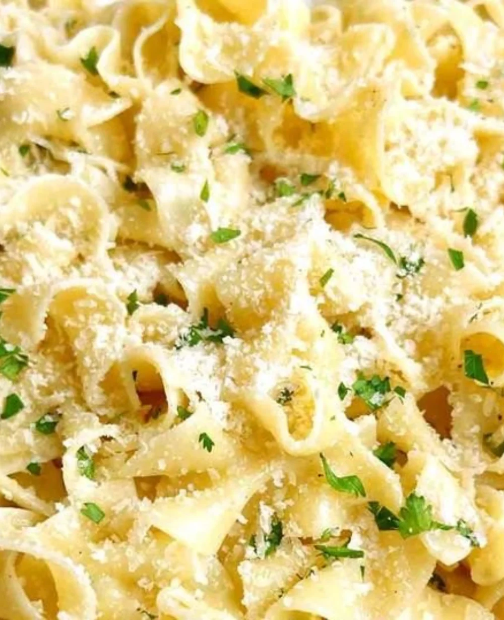Plate of creamy buttered noodles garnished with parsley on a wooden table.