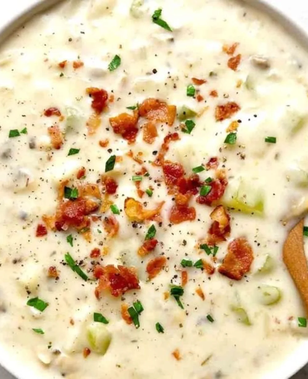 Bowl of creamy clam chowder topped with herbs and served with a crusty bread roll.