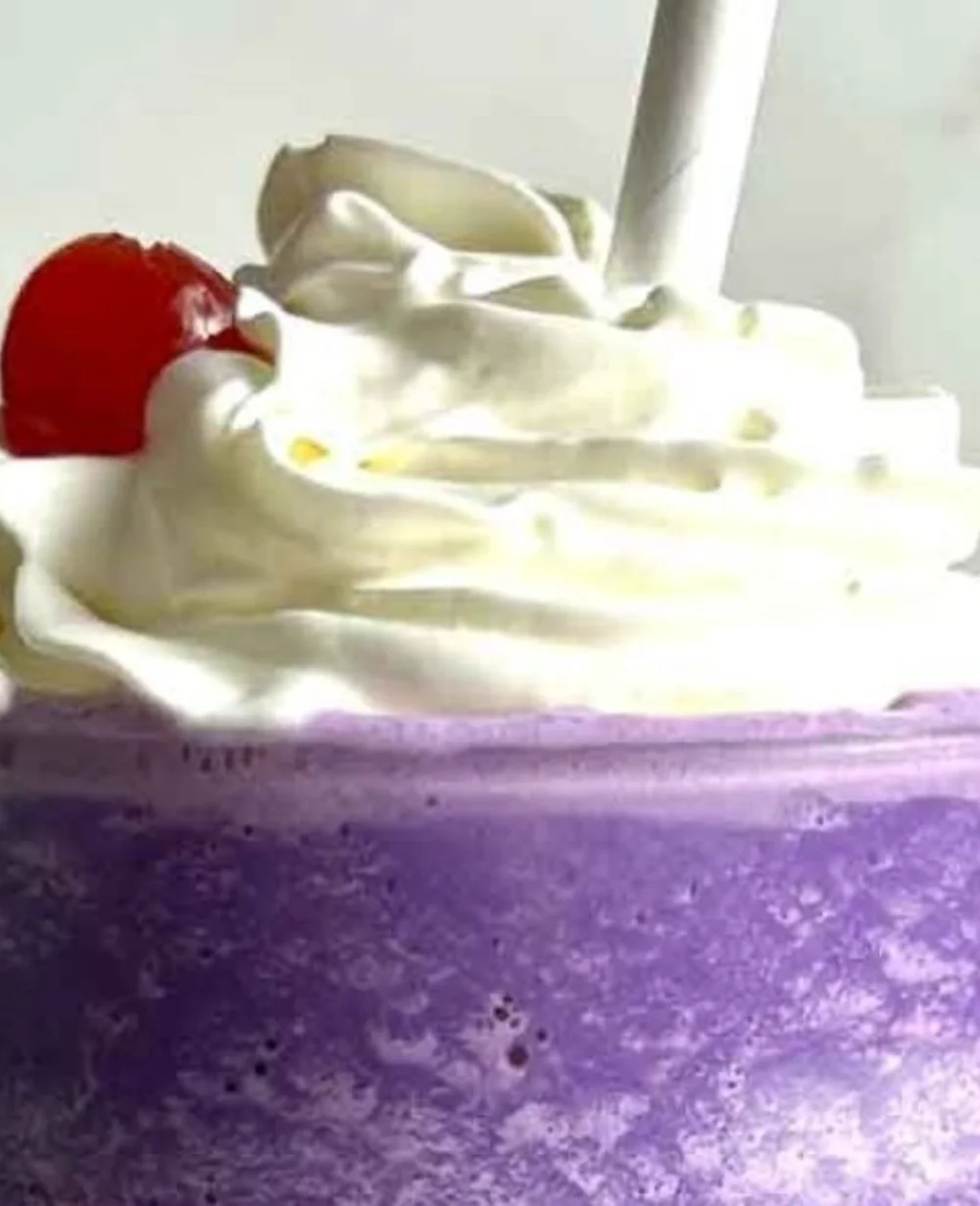 Creamy ube milkshake in a glass with whipped cream and a straw.