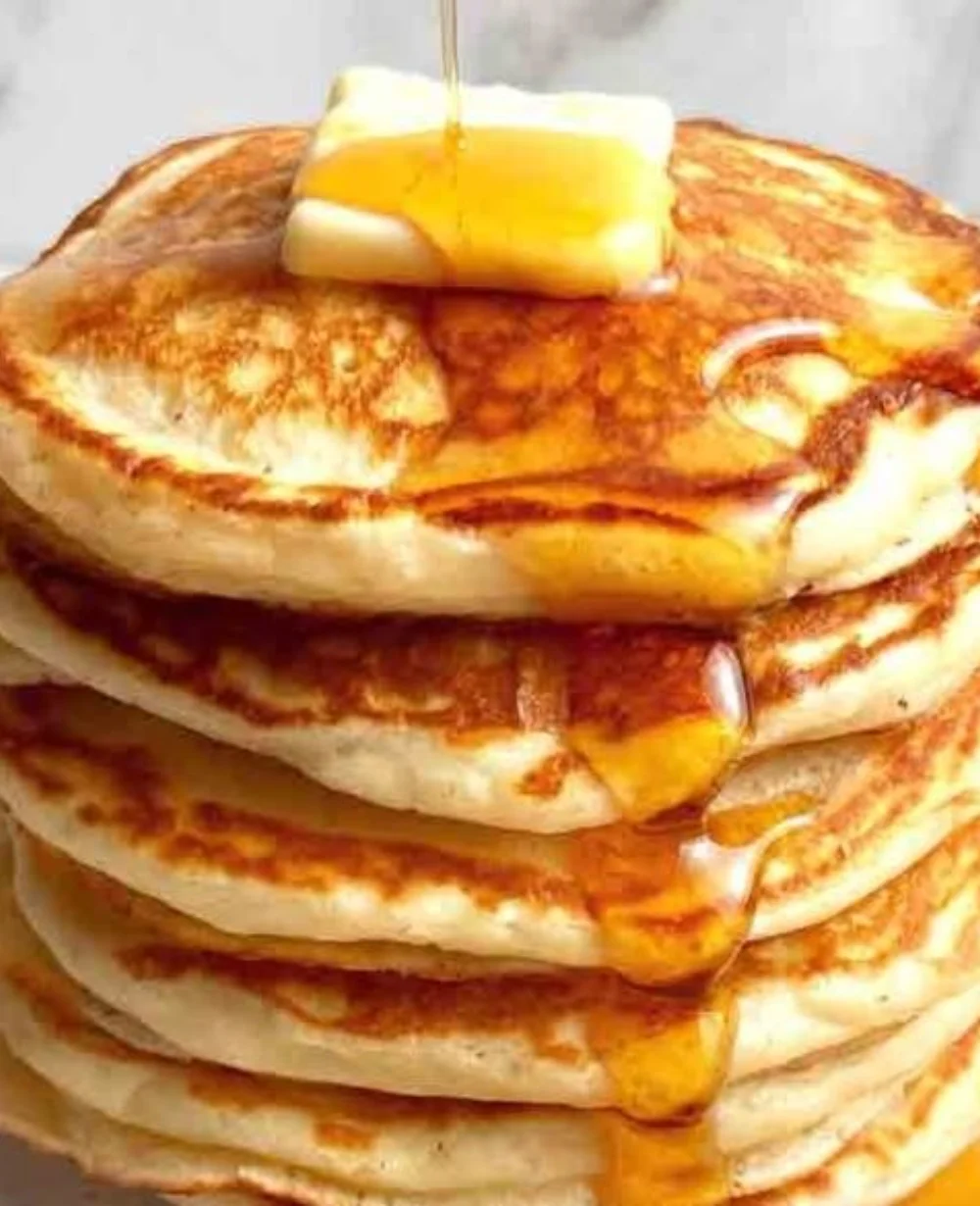 Fluffy Greek yogurt pancakes stacked on a plate with syrup and berries.
