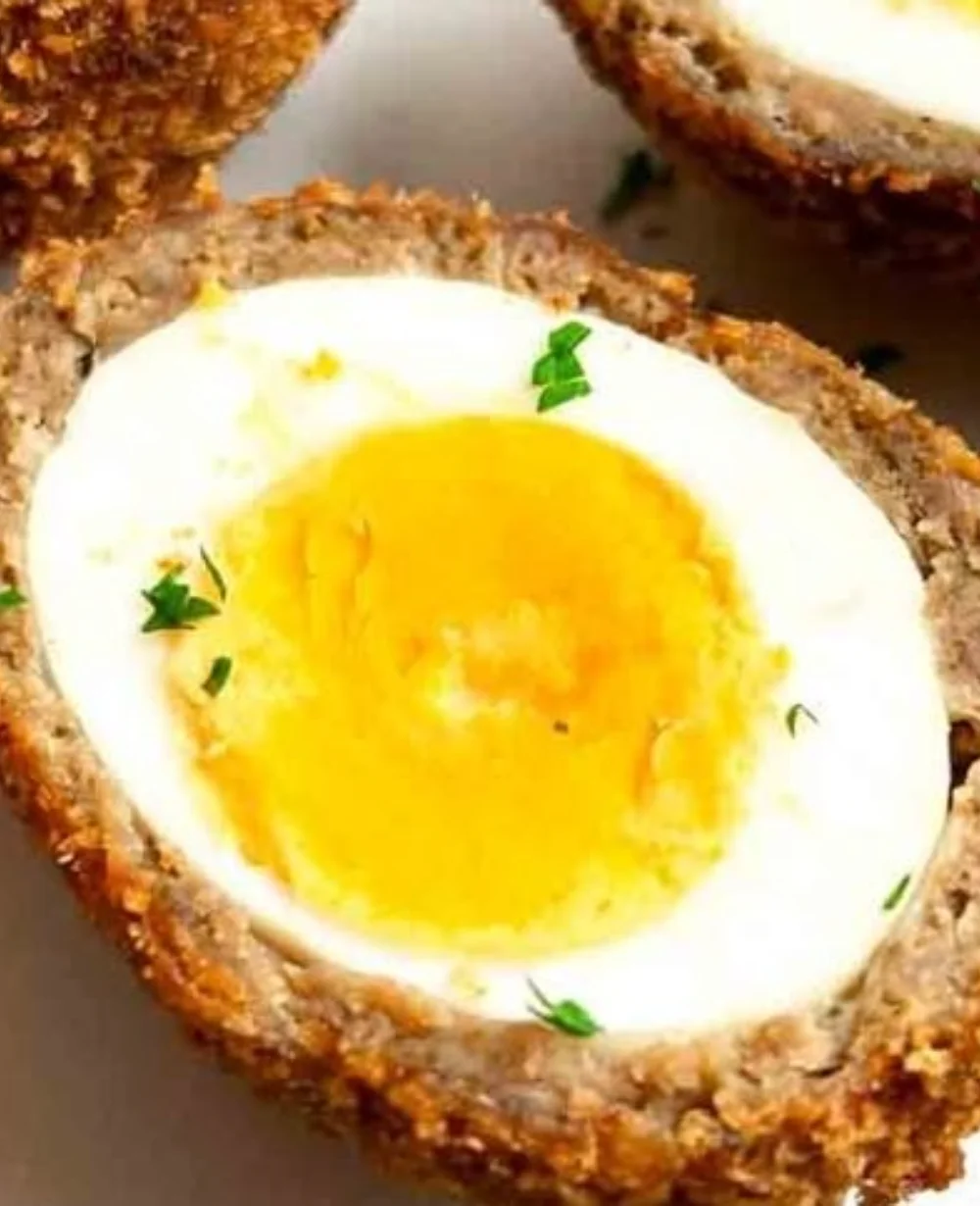 Homemade Scotch Eggs served with mustard on a wooden platter.