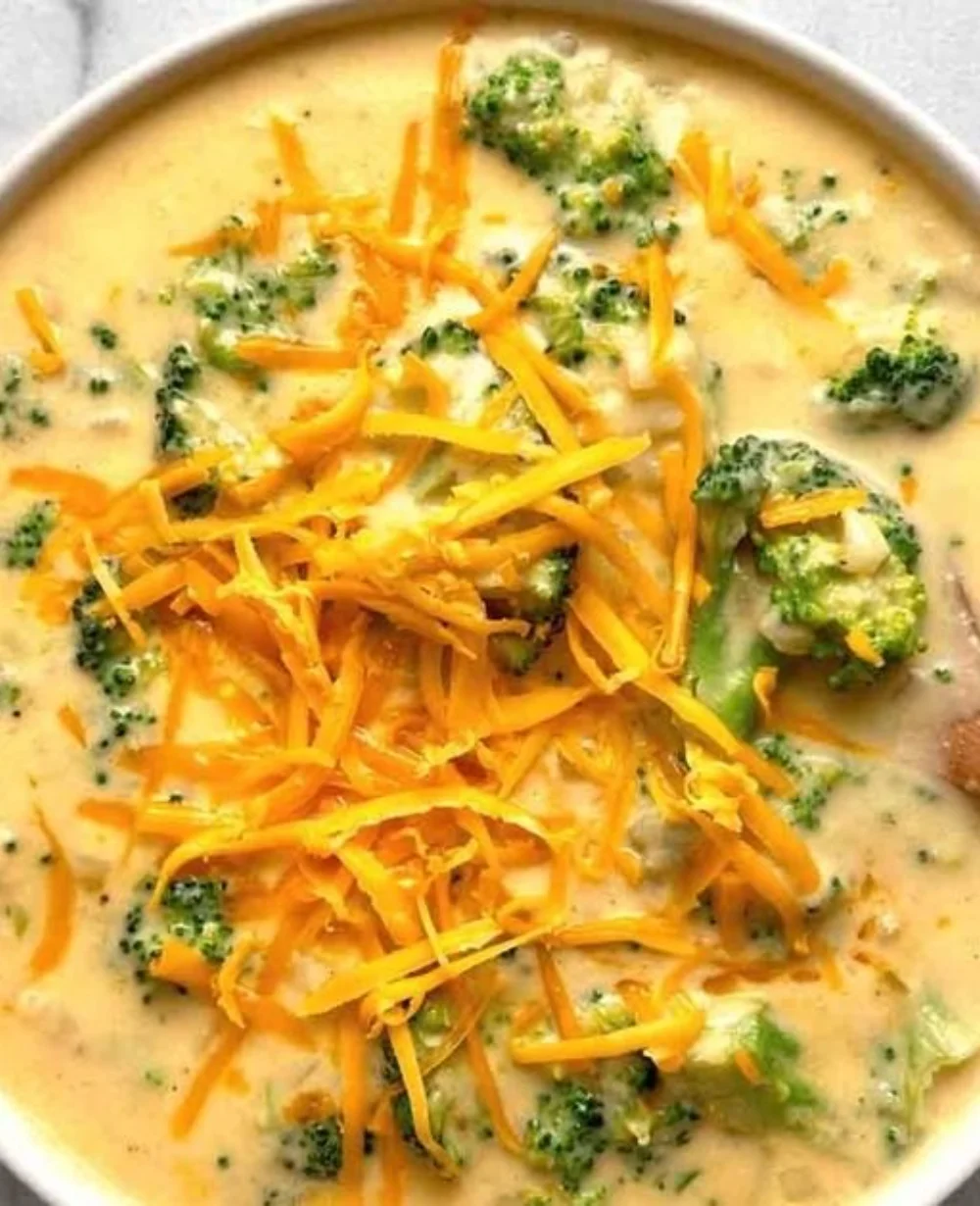 Bowl of creamy broccoli cheddar soup garnished with fresh herbs.