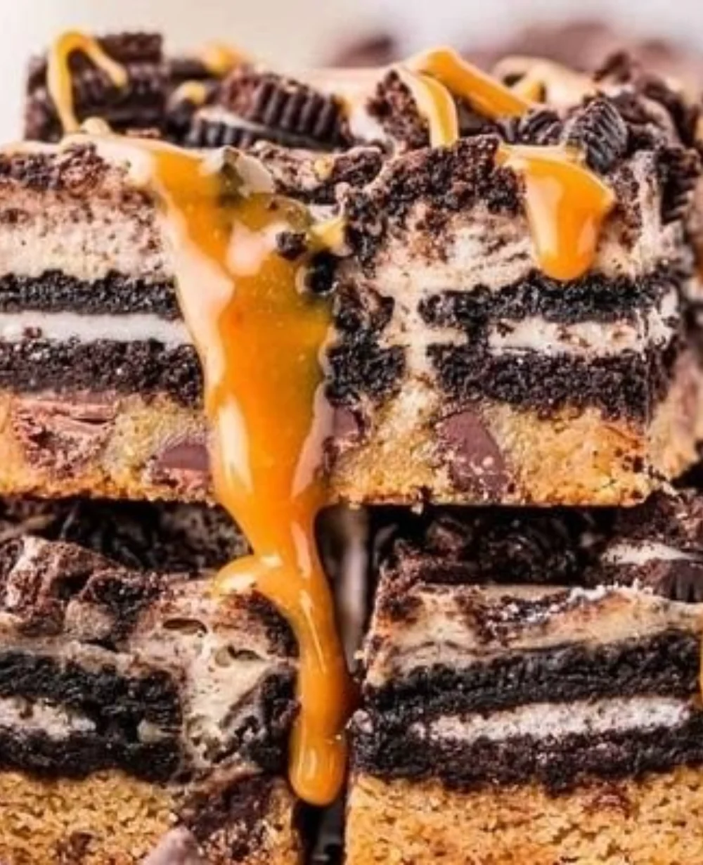 Delicious cheesecake bars topped with cookie crumbles and drizzled with chocolate.