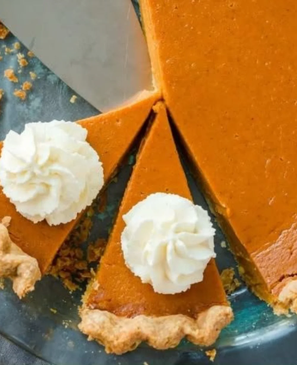 Delicious homemade pumpkin pie served on a wooden table with autumn leaves.