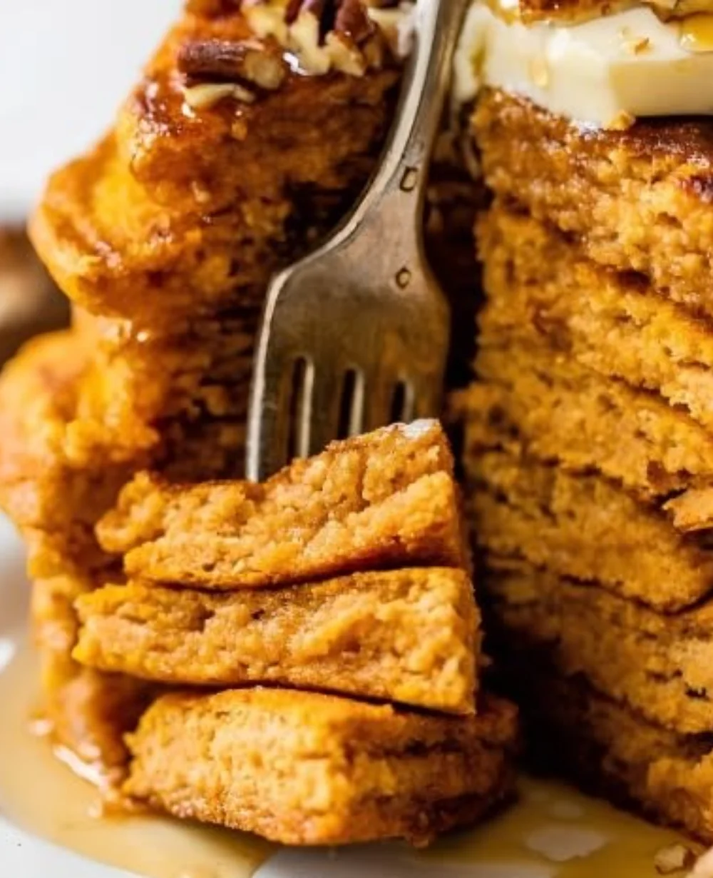 Fluffy easy pumpkin pancakes served on a plate with maple syrup and a sprinkle of cinnamon.