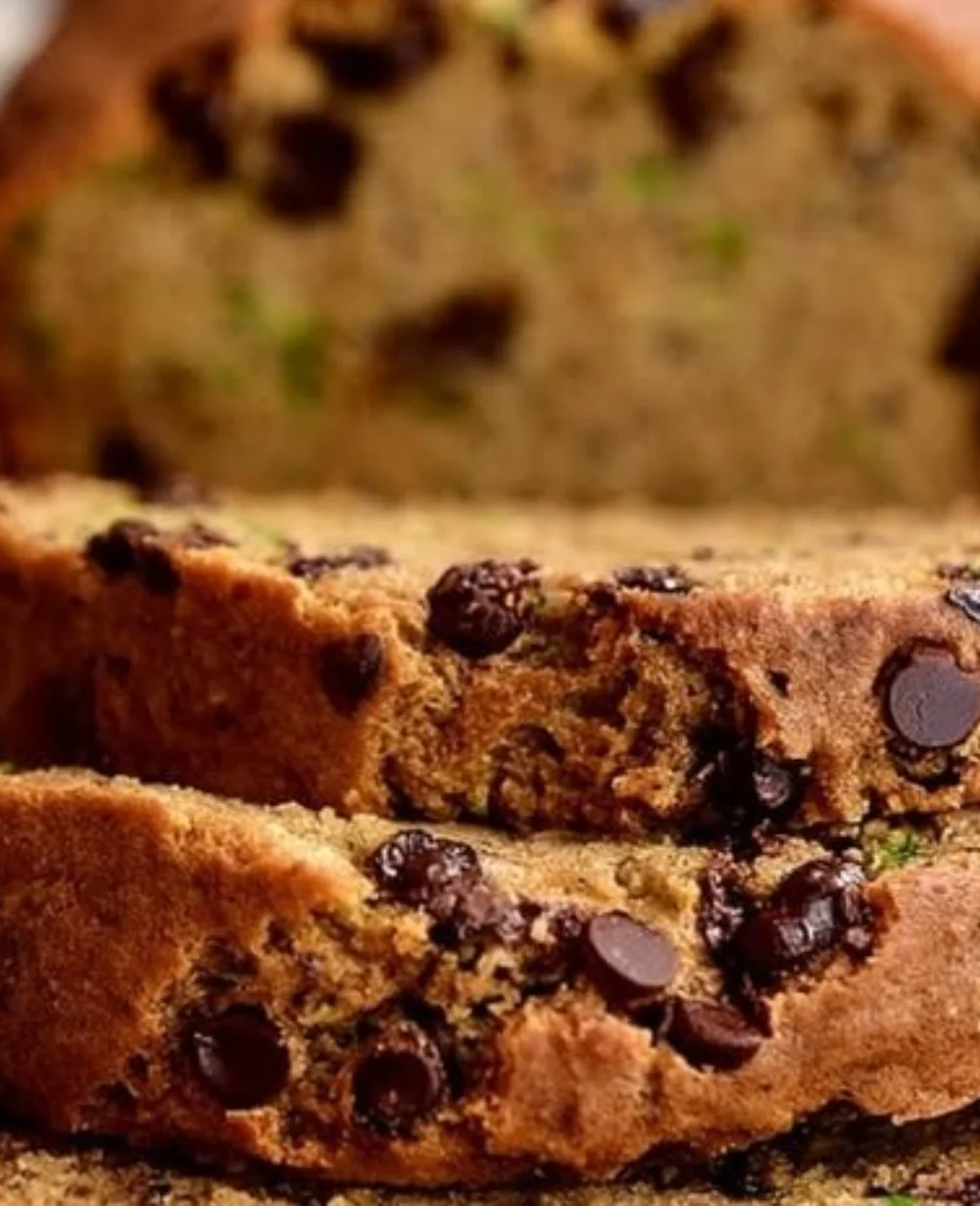 A slice of moist chocolate chip zucchini bread on a plate with chocolate chips visible.